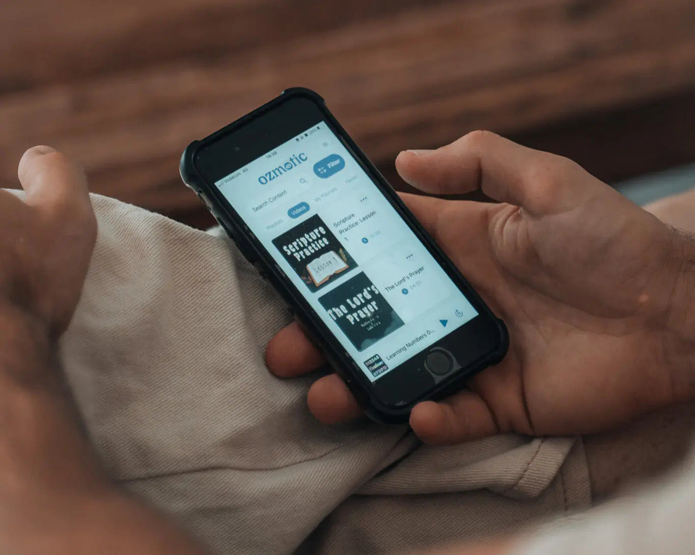 Close-up of a smartphone displaying the Ozmotic Learning app's content library, showing "Scripture Practice" and "The Lord's Prayer."