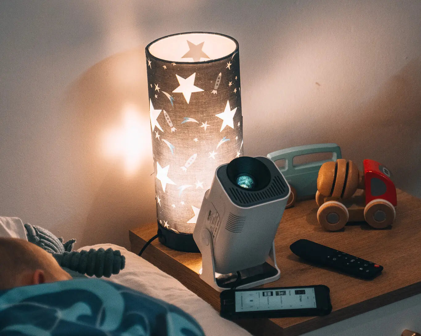 Ozmotic Learning projector sitting on a wooden nightstand next to a star-patterned lamp and toy truck.